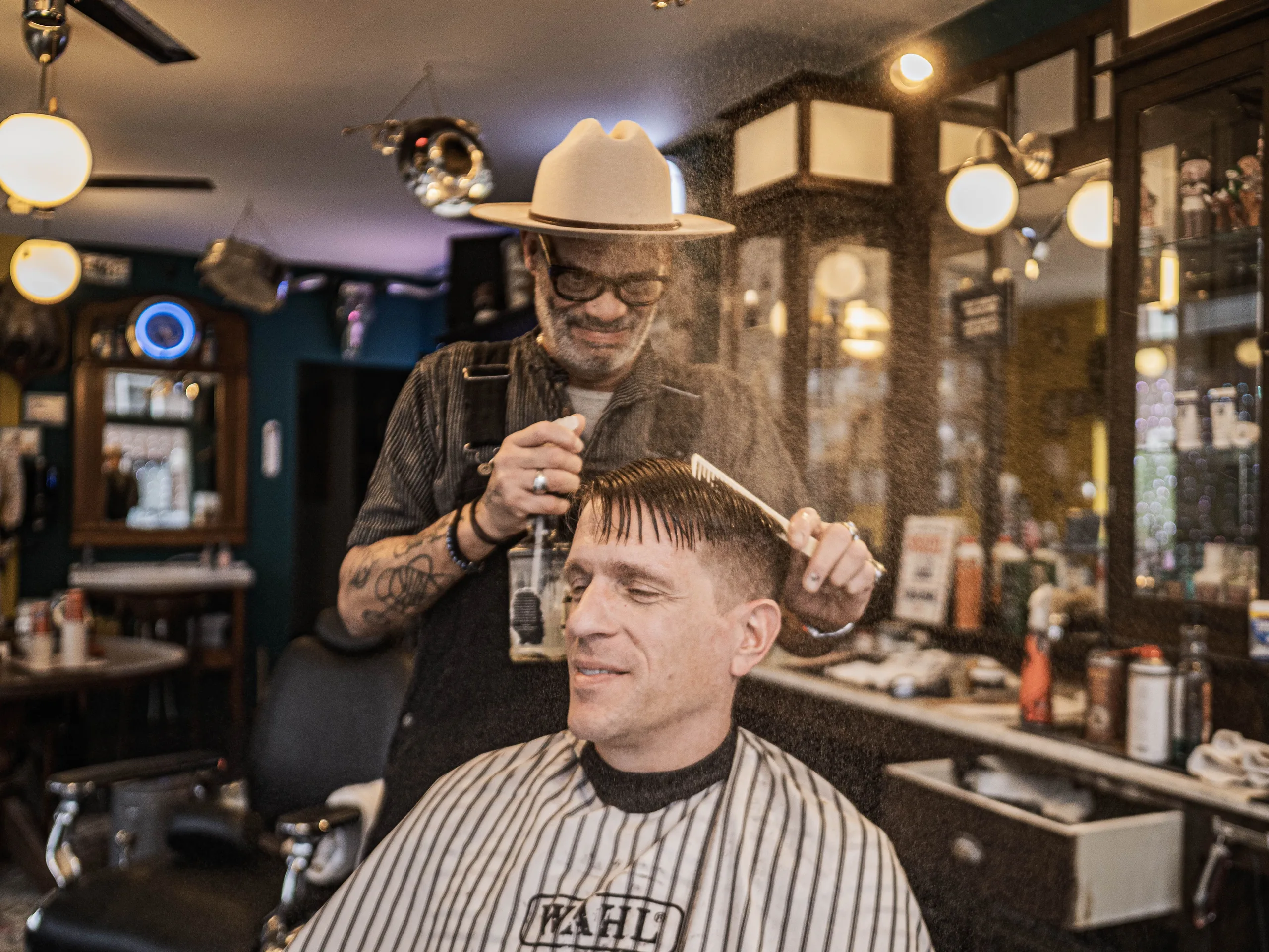 Barbier schneidet einem sitzenden Kunden im warm beleuchteten Salon die Haare